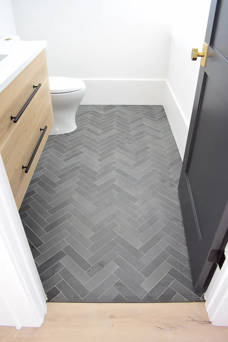 Grey herringbone bathroom tile next to a wooden vanity