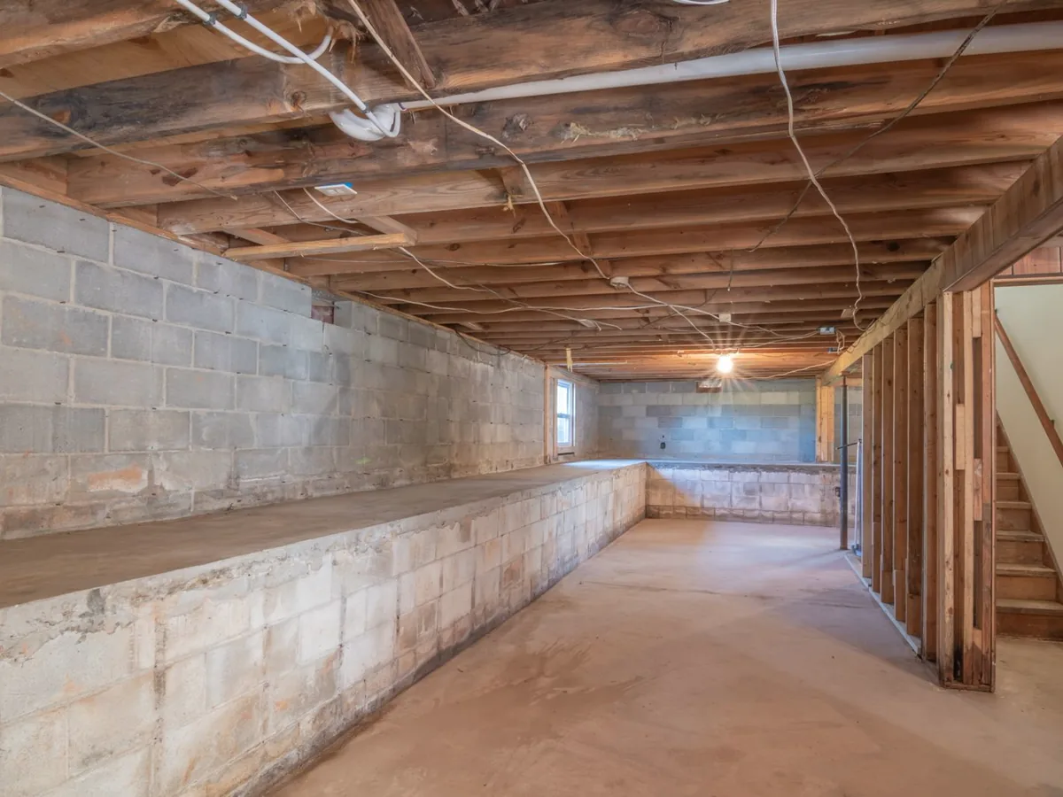 Unfinished basement with a bare concrete slab, block foundation walls and open floor joists overhead