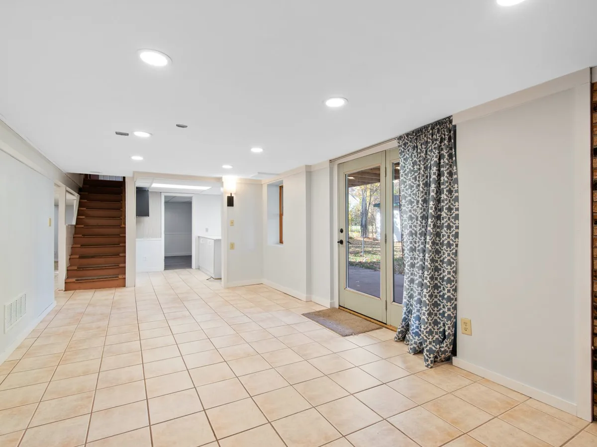 Walkout basement with beige ceramic tile floor, a glass patio door and stairs leading up