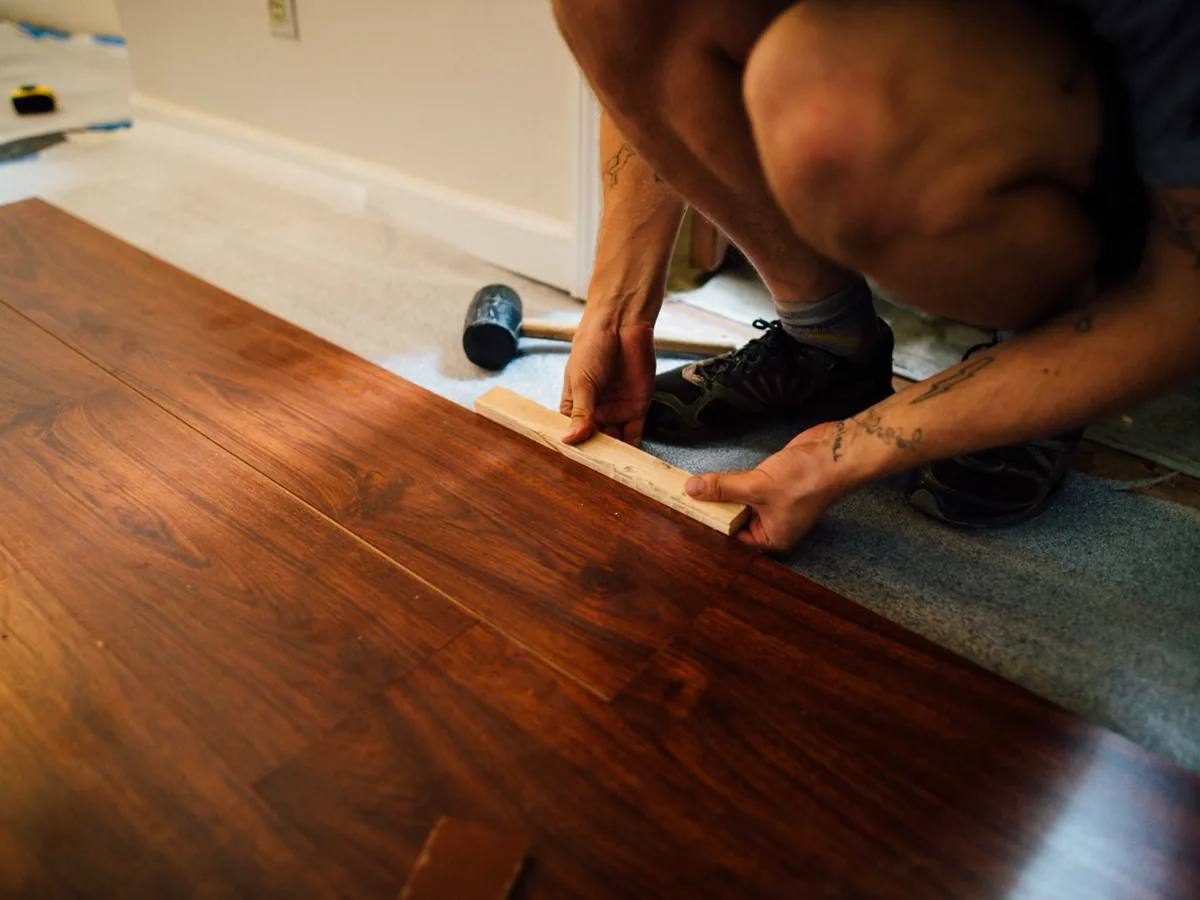 Installer tapping dark laminate planks together over a grey foam underlay