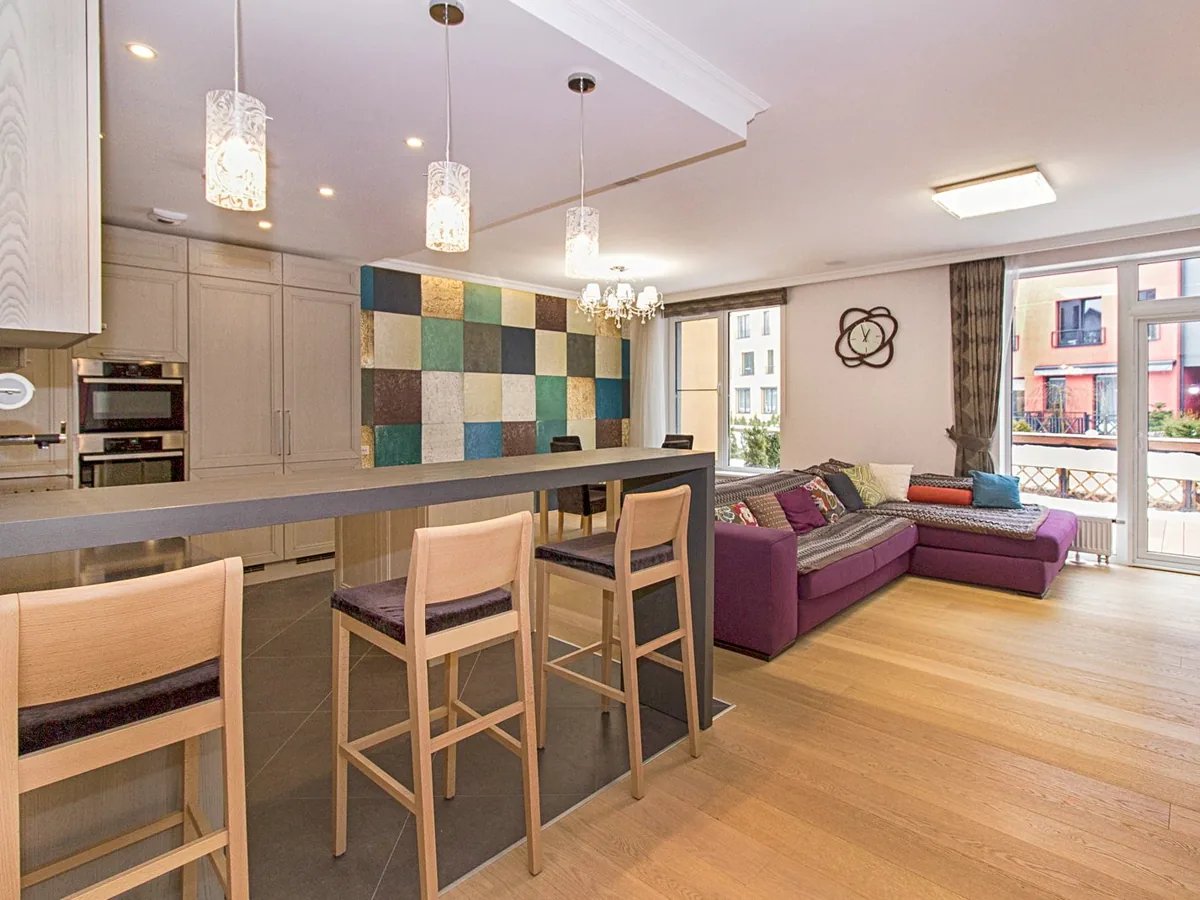 Open-plan condo kitchen and living room with light oak plank flooring and balcony doors