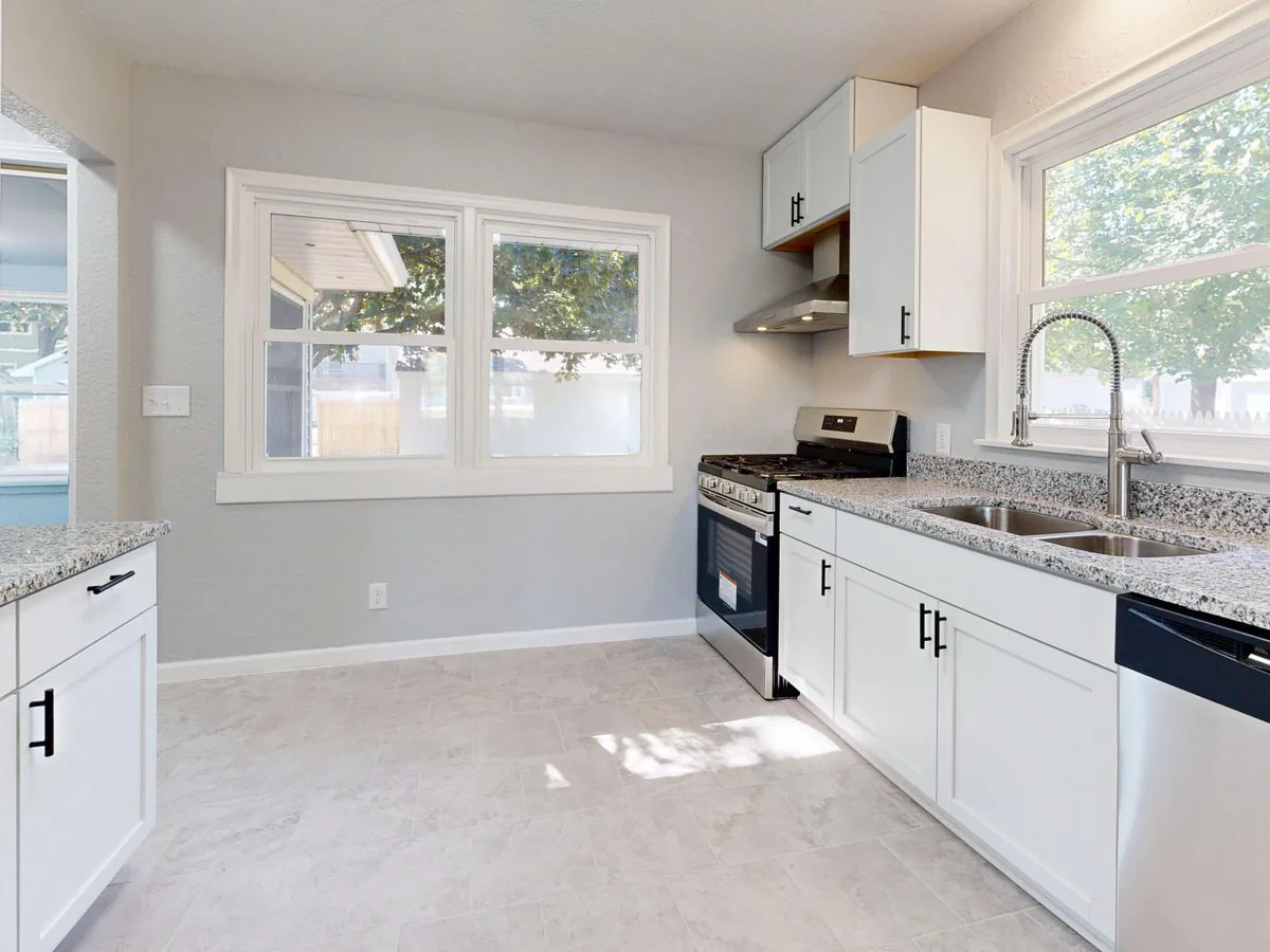 Bright kitchen with white cabinets, granite counters and a light grey large-format tile floor