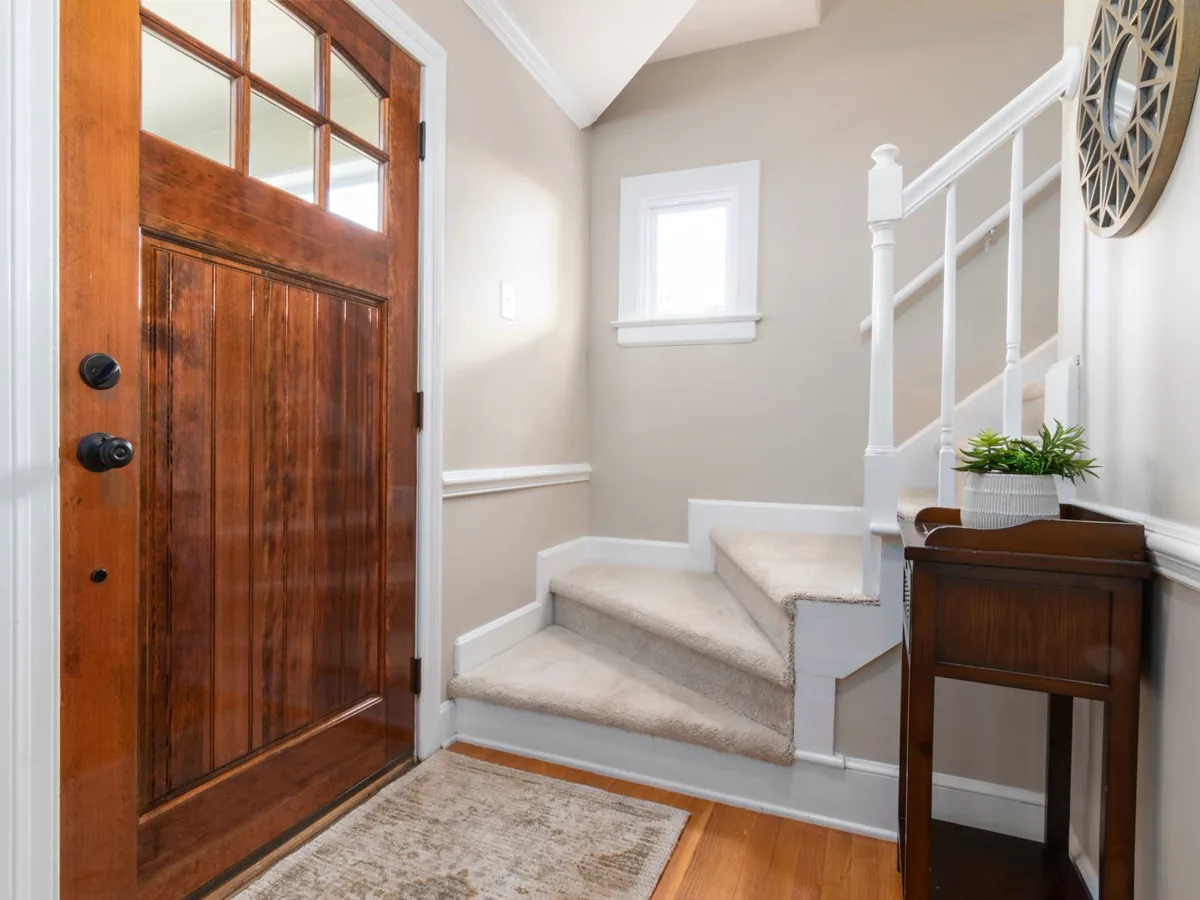 Carpeted staircase with white spindles turning at a landing beside a wooden front door
