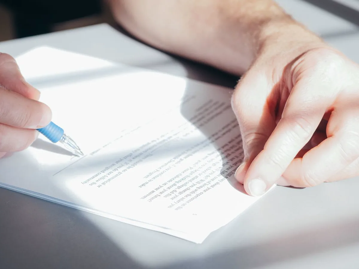 Hand signing a printed contract with a blue pen on a white desk