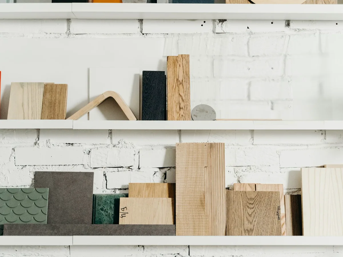 Wood plank samples in light and dark tones stacked on white shelves against a white brick wall